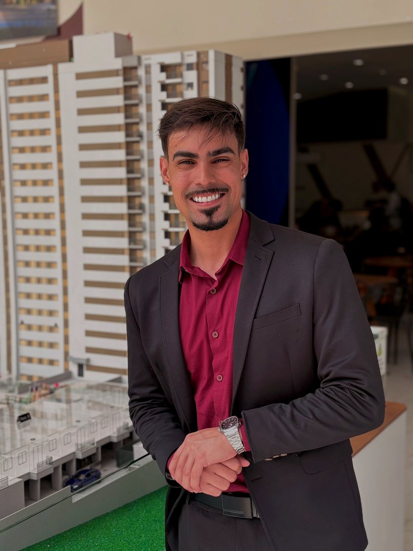 William Santos, corretor de imóveis, sorrindo diante da maquete de um empreendimento