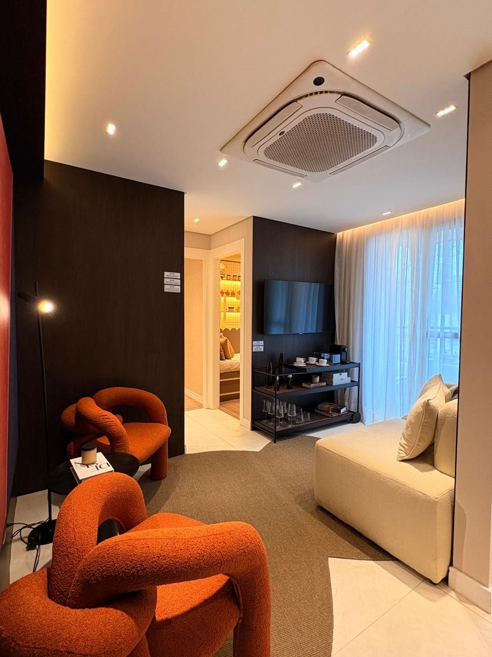 Sala de estar com poltronas laranja, sofá claro e TV