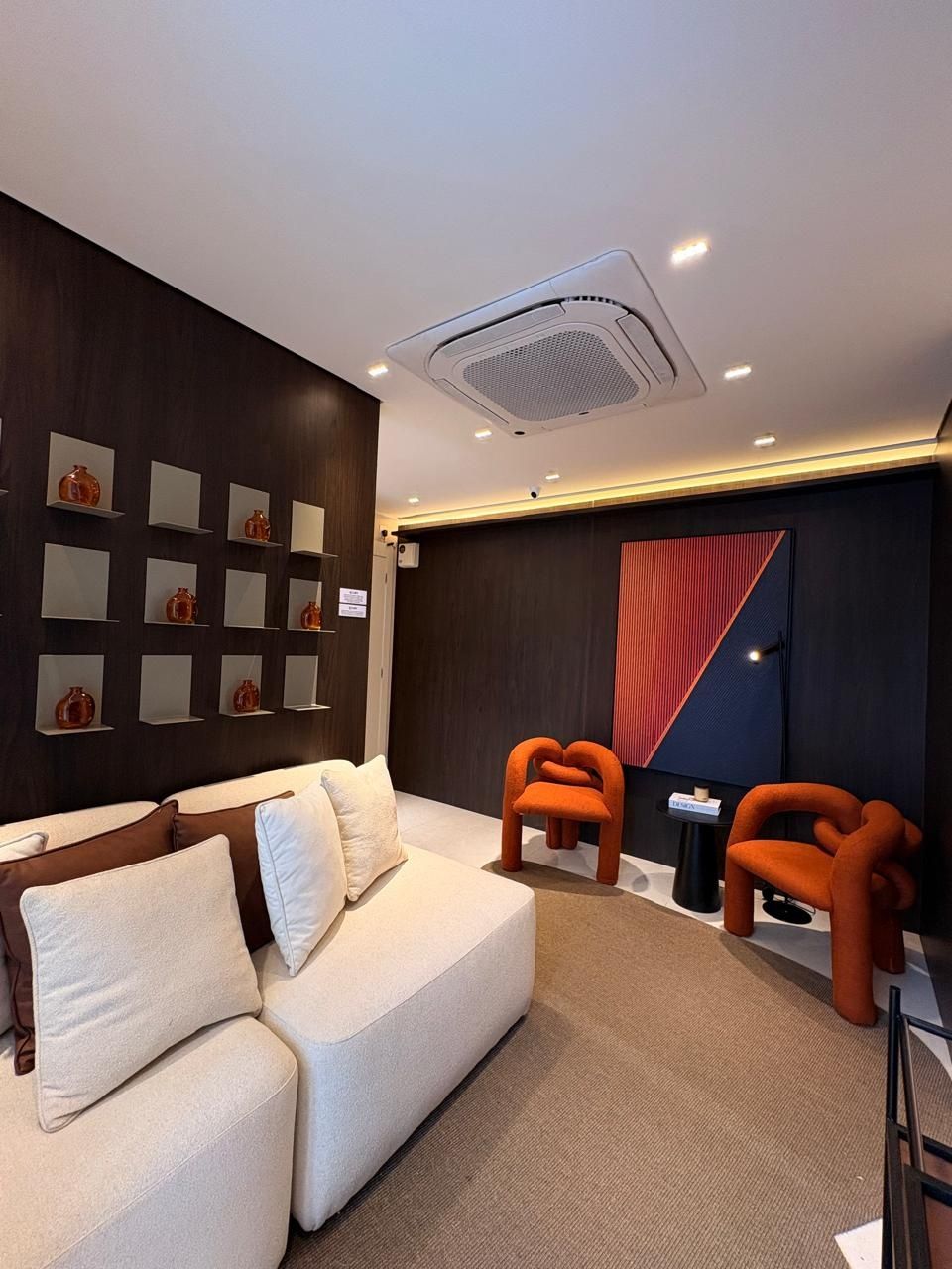 Sala de estar com sofá claro, nichos na parede e poltronas laranja